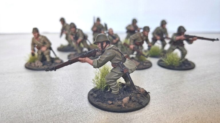 A squad of hand-painted 28mm WWII Japanese soldiers on custom round bases with stones and grass, focused on a rifleman in the foreground