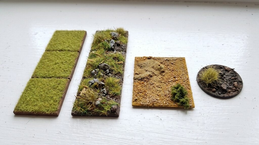 Four wargaming bases showing static grass, tufts, rocks, and bare earth texturing techniques