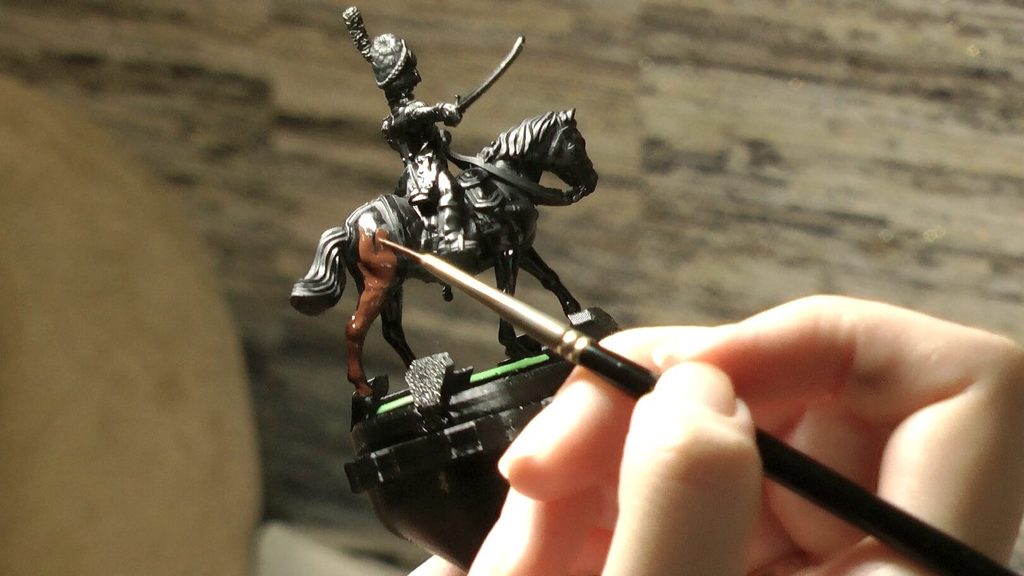 Close-up of a brush applying paint to a horse miniature